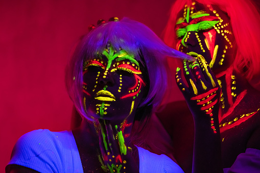 Portrait of two beautiful young women wearing fluorescent makeup.