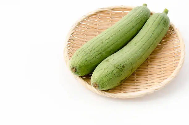 fresh green sponge gourd or loofah on a bamboo sieve on white background