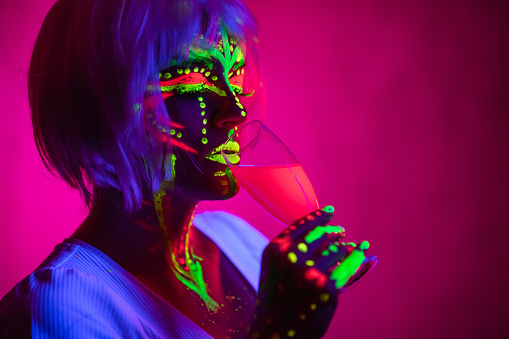 Portrait of a beautiful young woman wearing fluorescent makeup and drinking a fluorescent drink.