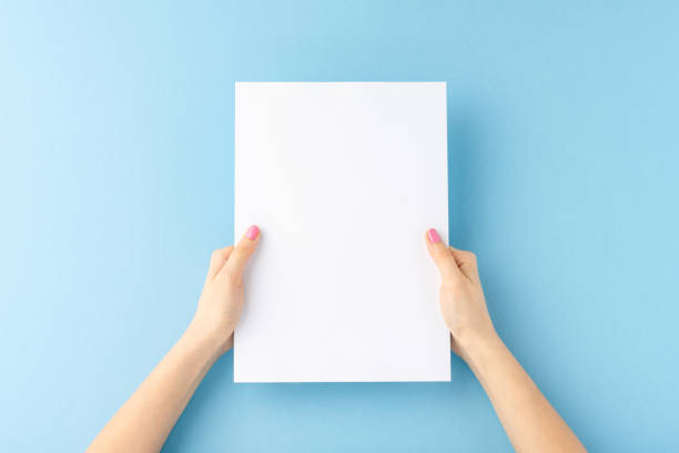 istock Young woman’s hands holding blank paper sheet on blue background. Mockup 1391776627