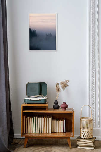 Vertical view of cozy living room with vinyl player on wooden sideboard with books, under art picture. Retro style decor, vintage furniture and analog or nostalgic sound equipment in apartment