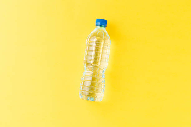 overhead shot of mineral water in small plastic bottle on yellow background with copyspace - plastic fles klein stockfoto's en -beelden