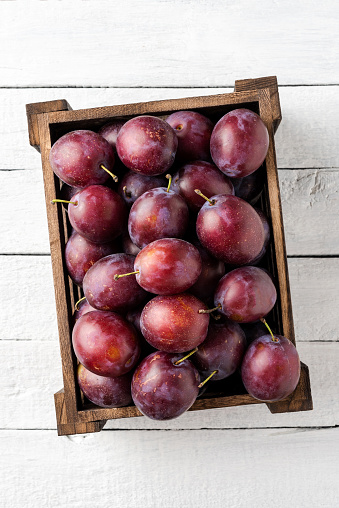 Overhead shot of plums in box on white wooden table. Close up