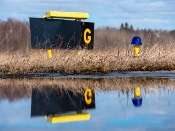 Closeup of a blue airport taxiway light with taxiway G sign in the background. Reflection on the water. stock photo