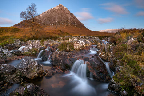 Famous Waterfall In Glencoe, Scotland, UK. Beautiful Scotland waterfall with blue sky and snowcapped mountain. Taken at Buachaille Etive mor, Glencoe, Scottish Highlands. buachaille etive mor photos stock pictures, royalty-free photos & images