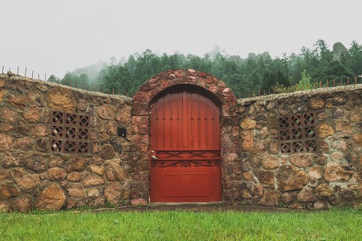 Red door in front of forest, rock walls