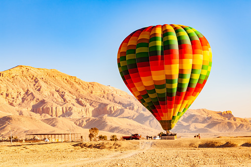 View of colorful hot air balloons with passengers landing on the plane at Valley of The Kings in the morning, Luxor, Upper Egypt.