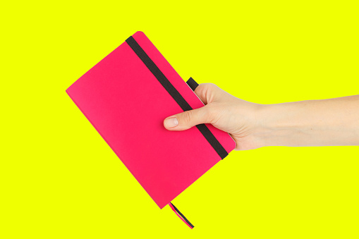 Pink notebook in the hand on the yellow background