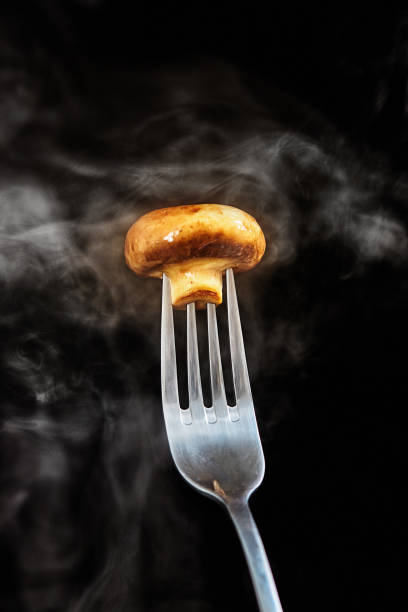 Steaming hot mushroom, impaled on a fork, held up against a black background