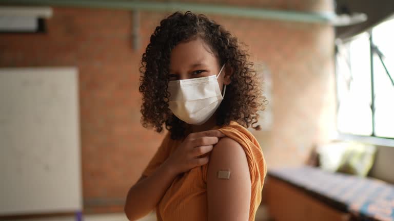 Portrait of a teenage girl showing her arm after vaccination - using a face mask