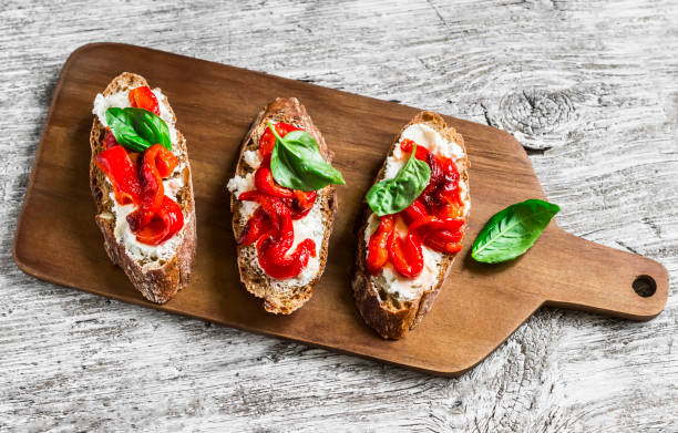 Bruschetta with feta cheese, roasted red sweet peppers and basil on a light wooden background Bruschetta with feta cheese, roasted red sweet peppers and basil on a light wooden background bruschetta stock pictures, royalty-free photos & images