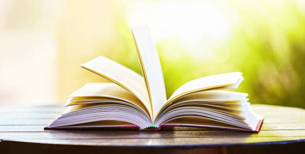 istock Open book on outdoor table in bright sunlight with dreamy blurred background 1391805522