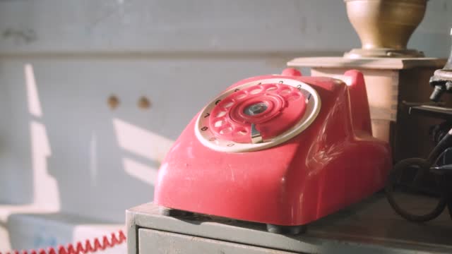 Caucasian women's hand dials a number on an old vintage red rotary phone close up. with sunset light in vintage room