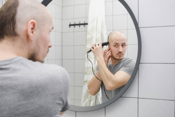 istock A man with hair loss problem cutting hair himself looking at mirror in the bathroom using trimmer. Baldness. 1391808436