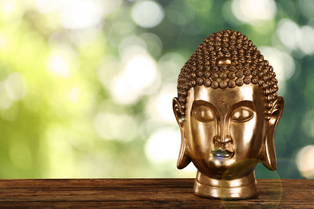 A contemplative stone Buddha statue rests peacefully, adorned with delicate flowers in its hollow center. The background features traditional colorful Tibetan prayer flags and a red monastery wall with Chinese characters for \