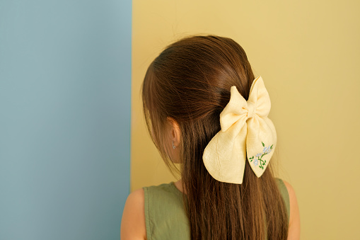 A beautiful big bow is an accessory for the hair on the girl's head. Long strong silky well-groomed brunette hair. A child on a yellow-blue studio background