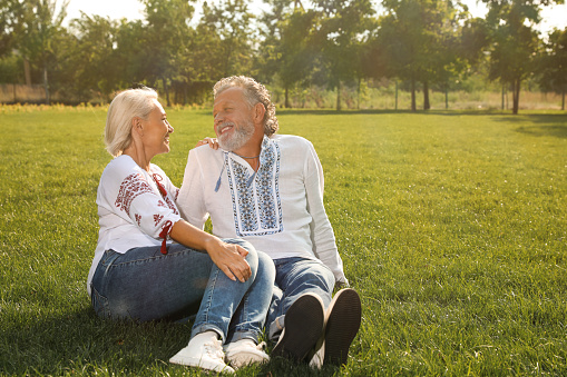 Happy mature couple in Ukrainian national clothes resting on green grass outdoors