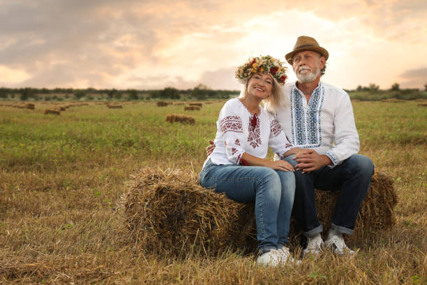 フィールドの干し草の俵にウクライナの国民服を着た幸せな成熟したカップル - husband wife couple senior adult ストックフォトと画像