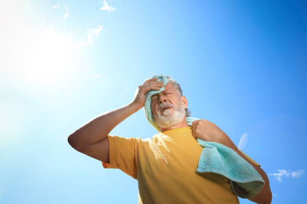 senior man with towel suffering from heat stroke outdoors, low angle view - exaustão imagens e fotografias de stock