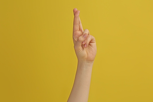 Mujer mostrando los dedos cruzados sobre fondo amarillo, primer plano photo