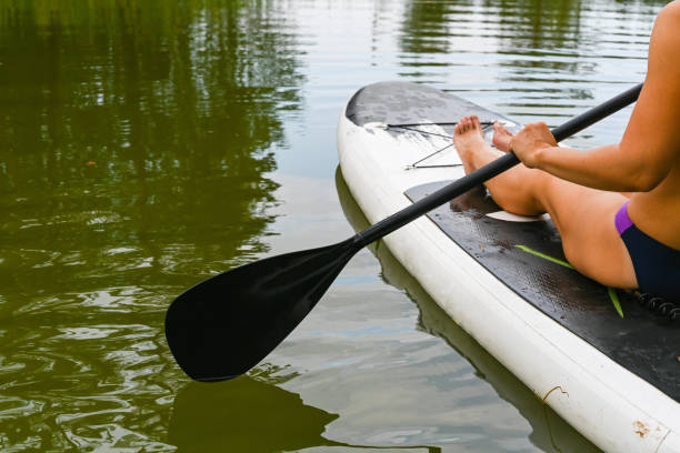 istock A woman drives on the Sup Board through a narrow canal surrounded by dense grass. Active weekend vacations wild nature outdoor. A woman is sitting in a swimsuit with her legs stretched out. 1391811044