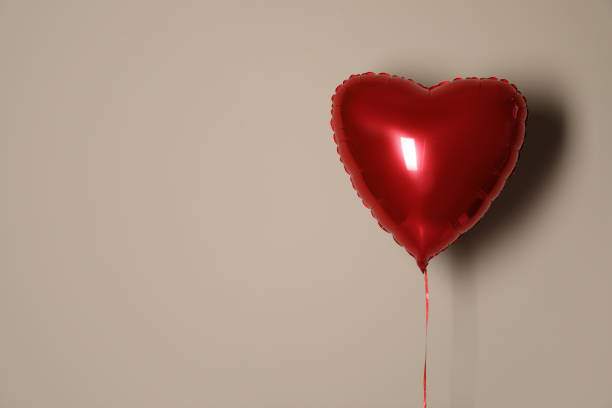 Festive heart shaped balloon on beige background. Space for text