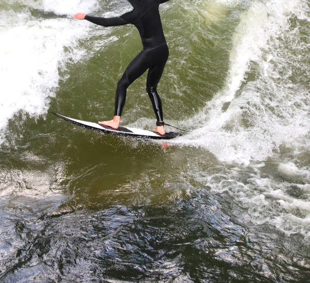 atleta surfista com roupa de mergulho cavalga as ondas enquanto se mantém em equilíbrio - englischer garten - fotografias e filmes do acervo