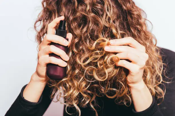 Close-up young woman spraying cosmetic oil on her naturally curly hair