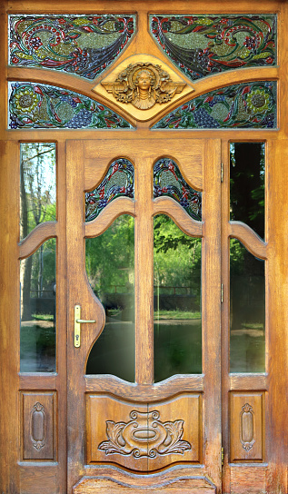 art nouveau design door, with colored glass, decorative figures engraved on wood and beautiful ornaments like the wooden sculpture of the head of a woman - entrance of an antiquarian store