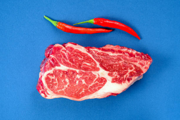 świeży surowy stek wołowy z czerwoną papryczką chili na niebieskim tle z bliska - bark abstract close up color image zdjęcia i obrazy z banku zdjęć
