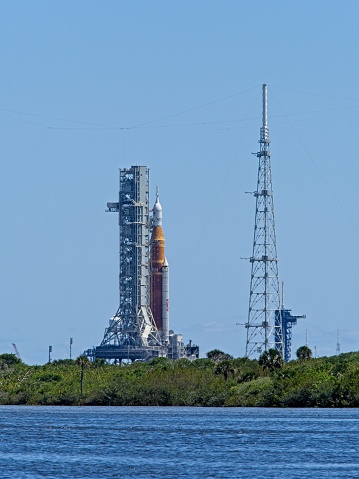 Artemis I, the first test of NASA's Space Launch System heavy lift vehicle sits on launch pad 39A at Kennedy Space Center on  April 11 2022. The space vehicle waits before another attempt at the wet dress rehearsal in April, before the actual launch and flight later in the spring. The SLS will carry the Orion capsule which will bring man back to the moon. The image at mid day shows the heat waves shimmering producing a slightly blurry view of the launch vehicle. View from across the many lakes and ponds of the Merritt Island national wildlife refuge.