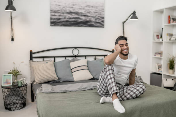 istock A man in white tshirt and plaid pants sitting on bed at home 1391823445