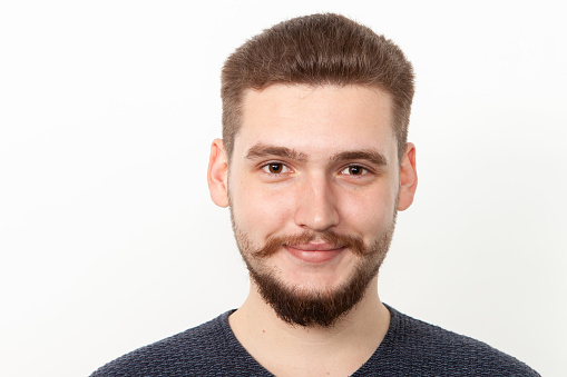 Close-up studio portrait of a 22 year old bearded man in a blue sweater on a white background