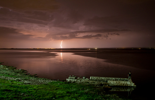 person watching a thunderstorm at night on the lake
