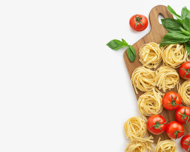 istock culinary background. Wooden kitchen board with raw pasta, tomatoes and basil on a light gray background 1391829317