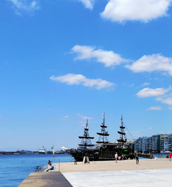 Thessaloniki, Greece - July 11, 2019: People walking on the coast in Thessaloniki. You see Thessaloniki seafront, Greece. Multistory buildings and the White tower, people relaxing on the promenade by the sea.