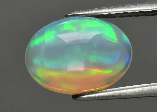 Natural gemstone opal in tongs on background