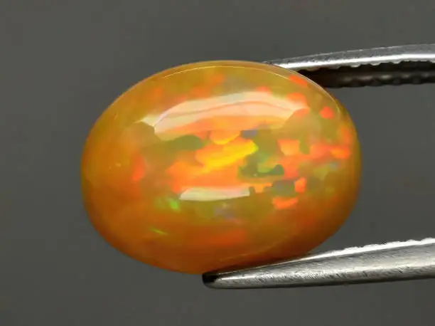Natural gemstone opal in tongs on background