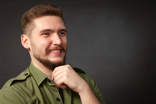 Close-up studio portrait of a 22 year old bearded man in a green shirt on a black background