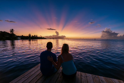 A male and female couple watching sunset over the island of Moorea from a pier near Papeete on Tahiti.
