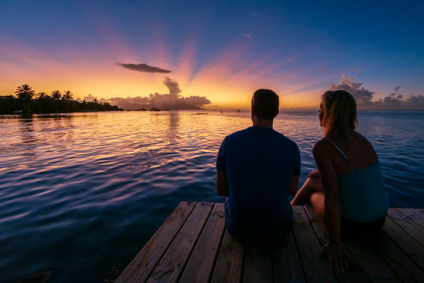 A male and female couple watching sunset over the island of Moorea from a pier near Papeete on Tahiti.
