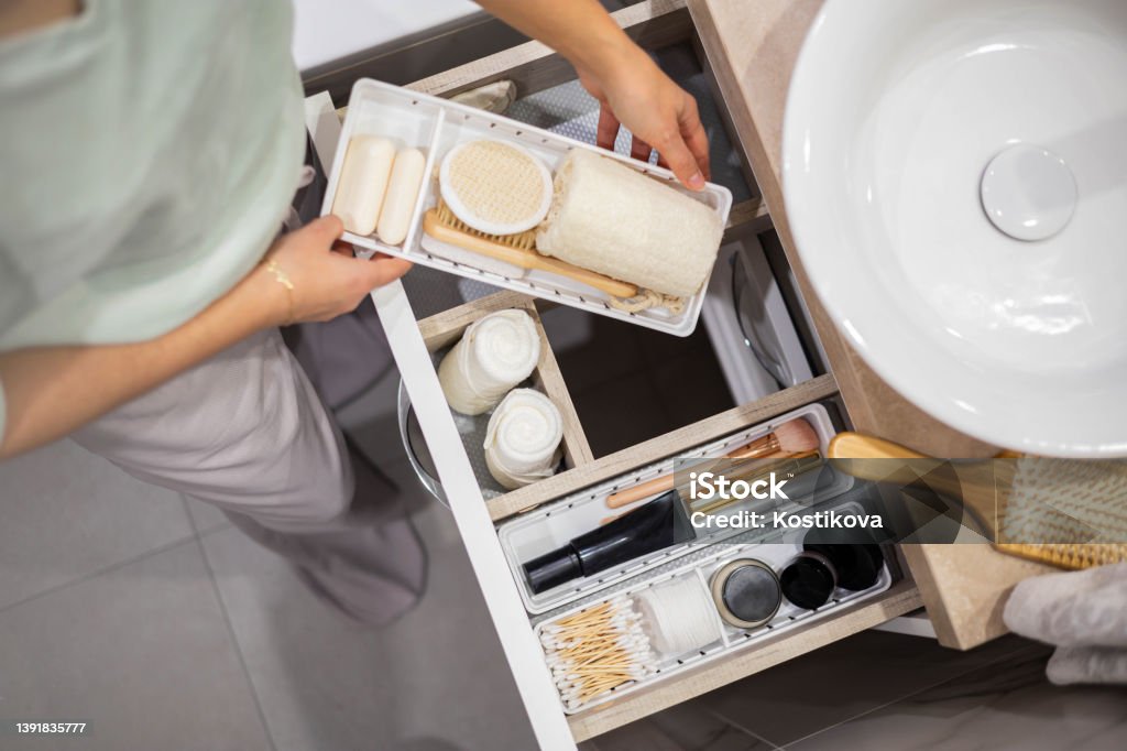 Top view of woman hands neatly organizing bathroom amenities and toiletries in drawer in bathroom Top view of woman hands neatly organizing bathroom amenities and toiletries in drawer or cupboard in bathroom. Concept of tidying up a bathroom storage by using Marie Kondo's method. Bathroom Stock Photo