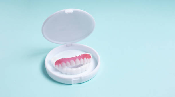 istock Full removable plastic denture in box on a blue background. Two acrylic dentures. Upper and lower jaws with fake teeth. 1391844451