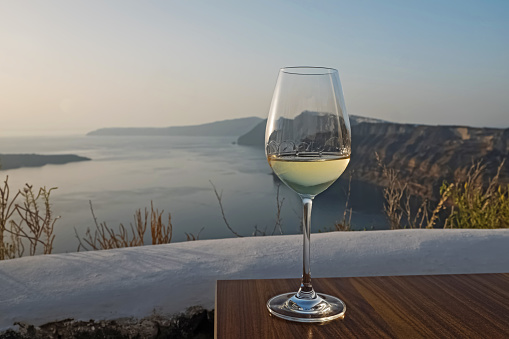 Glass of a white wine standing on the table with a view to Santorini caldera.