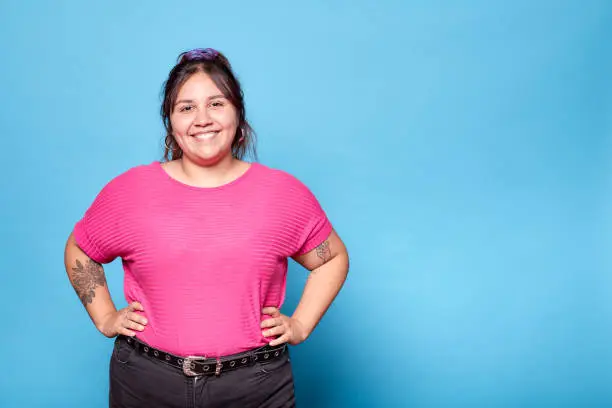 Photo of Young curvy latina woman smiling looking at camera isolated on turquoise background. Copy space.