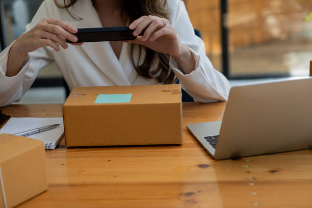 young woman selling online and using cell phone and laptop at her work, starting a small business, freelance asian sme entrepreneur with post box, packaging, online marketing and delivery. - post processing imagens e fotografias de stock