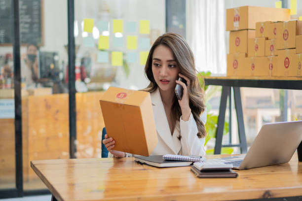 istock Young woman selling online and using cell phone and laptop at her work, starting a small business, freelance Asian SME entrepreneur with post box, packaging, online marketing and delivery. 1391859059