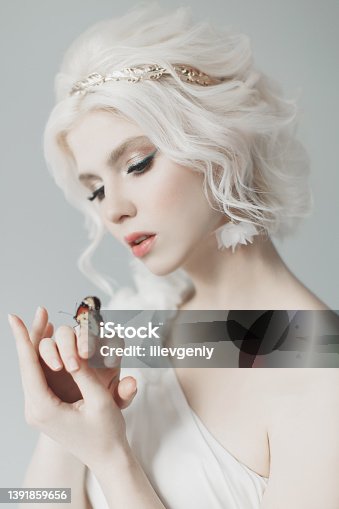istock Young blonde model in studio. Woman with beautiful luxurious greek hairstyle in white dress. Girl with butterfly on hand. Golden wreath. Albino. Beauty portrait. Greek goddess. Purity and innocence 1391859656