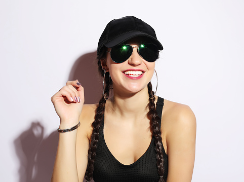 Portrait of a young woman in a cap and sunglasses over white background.Sporty stile.
