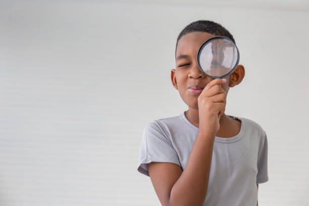 chłopiec trzymający lupę, mały chłopiec trzymający i patrzący przez szkło powiększające pokazujący wielkie oko - curiosity searching discovery home interior zdjęcia i obrazy z banku zdjęć